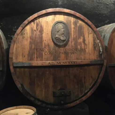 Ein großer Holzfass mit einer Medaille und der Inschrift „CAROLUS THEODORUS COMES PATRONUS A.D. MCMXXXXI“. Im Hintergrund sind weitere Fässer sichtbar.