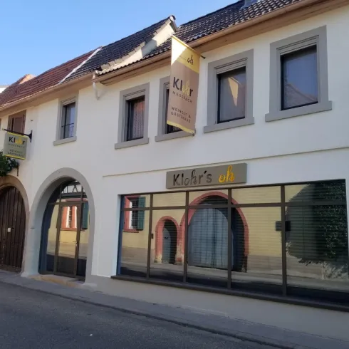 Ein modernes Gebäude mit einer einladenden Fassade. Es zeigt das Schild "Klohr's" und hat große Fenster mit grünen Pflanzen.