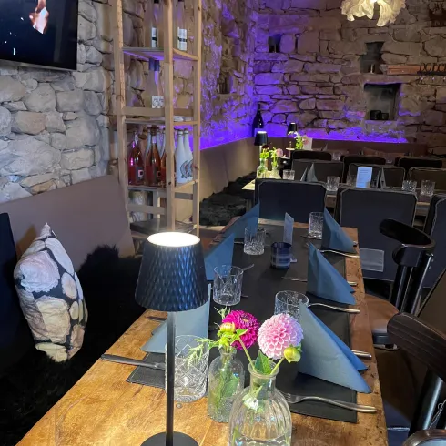 Ein modernes Restaurant mit einem holzigen Tisch und elegantem Geschirr. Sanfte Beleuchtung und frische Blumen schaffen eine einladende Atmosphäre.