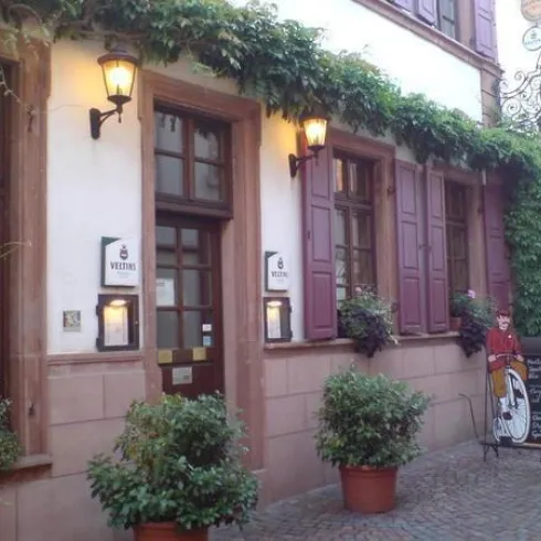 Eine charmante Restaurantfassade mit blühenden Pflanzen und zwei Laternen. Neben den Türen steht ein Schild mit einem Menü.