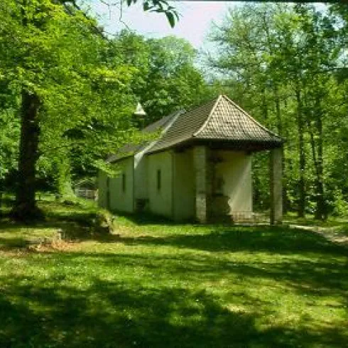 Ein kleines, malerisches Gebäude umgeben von grünen Bäumen. Die Szene strahlt Ruhe und Natürlichkeit aus.