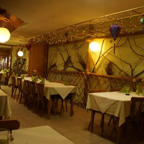 Ein gemütliches Restaurant mit Tischen, die mit weißen Tischtüchern gedeckt sind. Die Wände sind mit schönen Wandmalereien und dekorativen Beleuchtungselementen geschmückt.