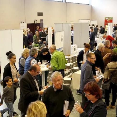 Eine geschäftige Messe mit vielen Menschen, die an Ständen interagieren. Es gibt zahlreiche Aussteller und Besucher, die sich über verschiedene Produkte informieren.