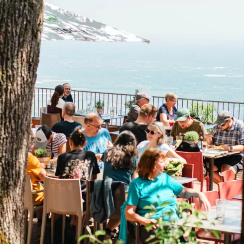Ein lebhaftes Restaurant im Freien mit vielen Gästen, die am Tisch sitzen und das Meer im Hintergrund genießen. Die Atmosphäre ist entspannt und einladend.