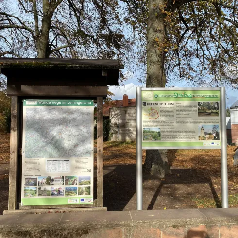 Zwei Informationsschilder in einem Park. Eines zeigt eine Karte, das andere bietet Informationen über die Umgebung.