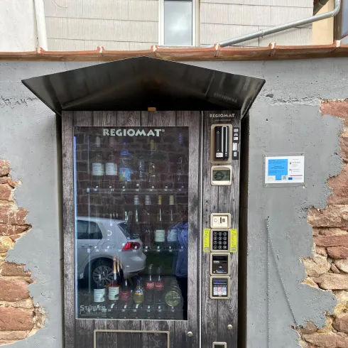 Ein Verkaufsautomat für Wein steht an einer Wand aus Stein. Er ist modern gestaltet und hat oberhalb eine Überdachung.