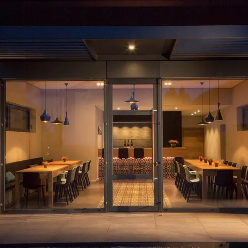 Ein modernes Restaurant mit großen Fenstern, das ins Innere mit einer warmen Beleuchtung blickt. Tische und Stühle sind ordentlich angeordnet, um eine einladende Atmosphäre zu schaffen.