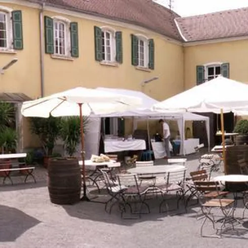 Der gepflasterte Innenhof des Weingut Winkels- Herding. Der Innenhof ist umgeben von einem gelben Gebäude und ausgestattet mit Schirmen und Außenbestuhlung.