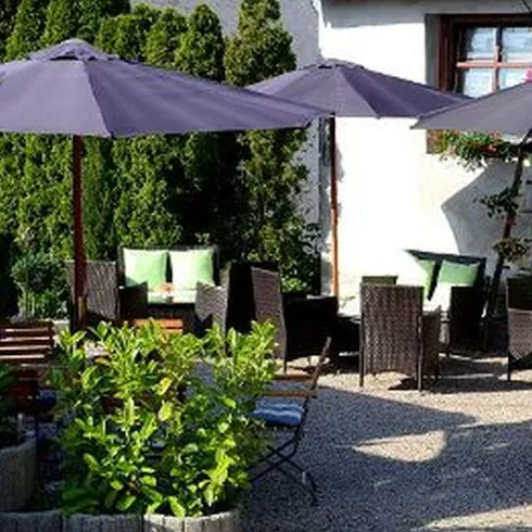 Eine gepflasterte Terasse mit dunkelen Sitzmöben. Die Terasse ist von einer Buschwand umgeben.