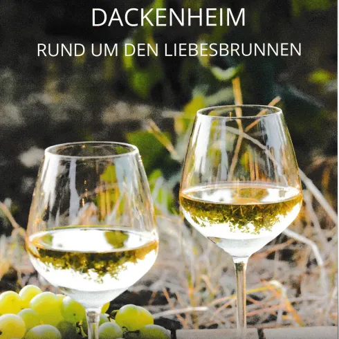 Zwei Weingläser mit weißem Wein stehen auf einem Tisch, umgeben von Trauben. Im Hintergrund sind grüne Blätter sichtbar.