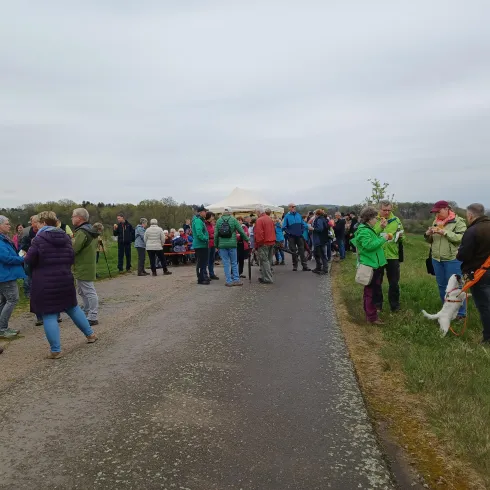 Eine Gruppe von Menschen versammelt sich auf einem Weg in der Natur. Es sind verschiedene Aktivitäten und Gespräche sichtbar, während einige Teilnehmer Radfahren oder sich unterhalten.