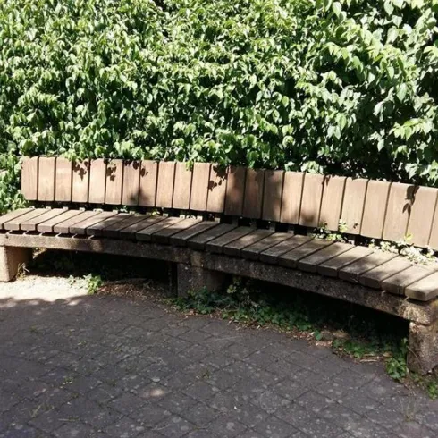 Eine angelegte Bank in einem grünen Bereich, umgeben von Sträuchern. Der Platz ist ruhig und einladend.