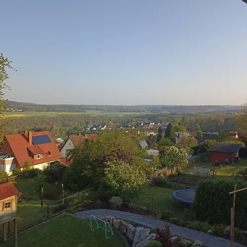 Eine ruhige Landschaft mit einem Blick auf ein Dorf und umliegende Felder. Die Häuser sind von Bäumen und Gärten umgeben.