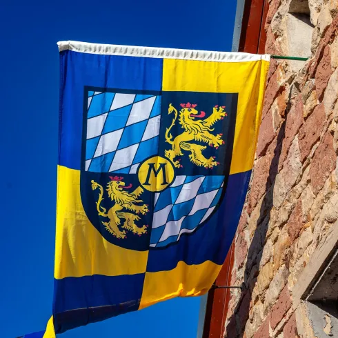 Eine Fahne weht vor strahlend blauem Himmel mit weiß-blauen Rauten und Pfälzer Löwe, das ist das Wappen von Meckenheim/Pfalz