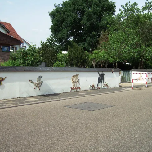 Eine lange Mauer ist mit bunten Tiermotiven bemalt. Zu sehen sind Schmetterlinge, Vögel und andere Tiere in einer lebendigen Umgebung.