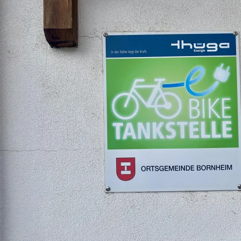 Ein Schild für eine E-Bike Tankstelle in der Ortsgemeinde Bornheim. Es zeigt ein Fahrrad und ein Ladekabel symbolisch.