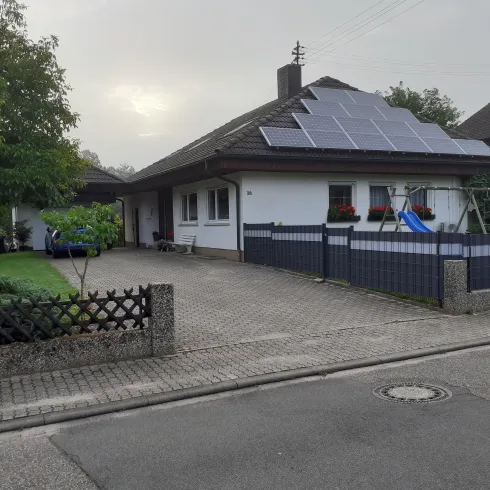Ein modernes Einfamilienhaus mit Solarpanelen auf dem Dach. Der gepflegte Garten und der Spielplatz im Vordergrund sorgen für eine einladende Atmosphäre.