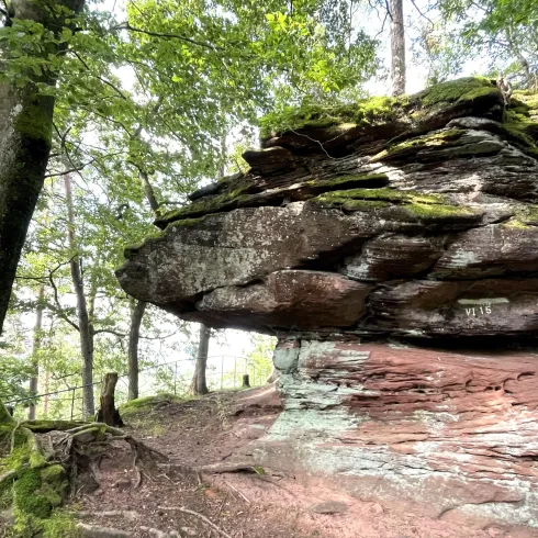 Ein beeindruckender Steinblock, der auf einem weiteren Felsen liegt, umgeben von Bäumen. Das grüne Moos verleiht der Szene einen natürlichen Charme.