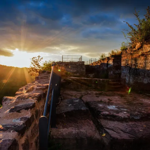 Eine alte Ruine im Sonnenuntergang mit sanften Lichtstrahlen. Im Hintergrund sind sanfte Hügel und ein klarer Himmel zu sehen.