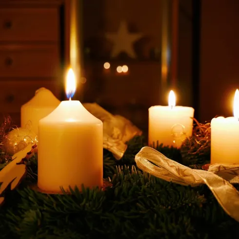 Ein festlicher Adventskranz mit vier brennenden Kerzen. Die warme Beleuchtung schafft eine gemütliche Atmosphäre.