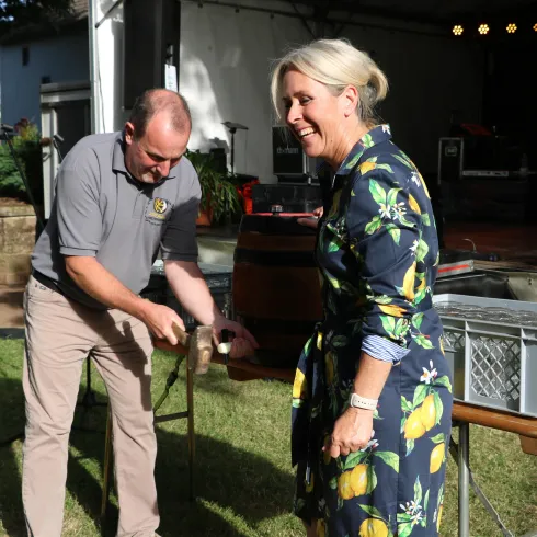 Ein Mann und eine Frau stehen in einem Garten. Der Mann hält einen Fisch, während die Frau lächelt und zuschaut.