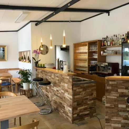 Ein modernes Café mit hellen Holzmöbeln und ansprechender Theke. Die Umgebung ist einladend und gut beleuchtet, mit Pflanzen und dekorativen Elementen.