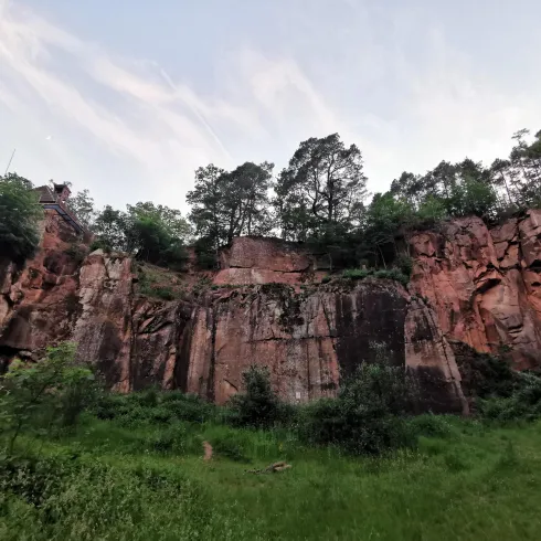 Eine beeindruckende Felsenlandschaft mit grünem Bewuchs und hohen Bäumen im Vordergrund. Der Himmel ist sanft und klar, was die natürliche Schönheit der Umgebung hervorhebt.