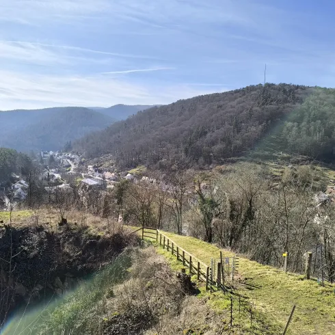 Eine malerische Landschaft mit sanften Hügeln und einem kleinen Dorf im Tal. Die Bäume sind spärlich und der Himmel ist klar und blau.