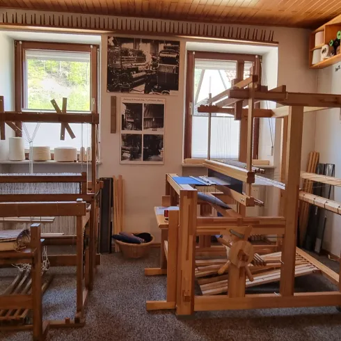 Ein traditioneller Raum mit Holzwebstühlen und Werkzeugen. Die Wände sind mit Bildern und Informationen über das Handwerk dekoriert.