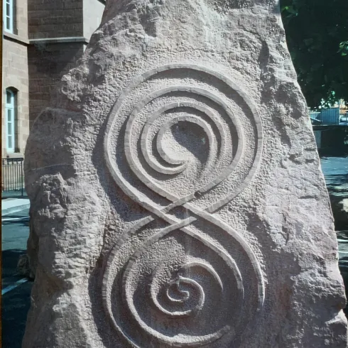 Ein großer, bearbeiteter Stein mit einer kunstvollen spiralförmigen Gravur. Die Gestaltung erinnert an eine liegende Acht.