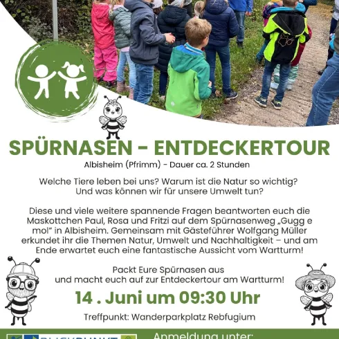 Eine Gruppe von Kindern und Erwachsenen steht in der Natur und erkundet die Umgebung. Es gibt Informationsschilder und die Veranstaltung heißt "Entdeckertour".