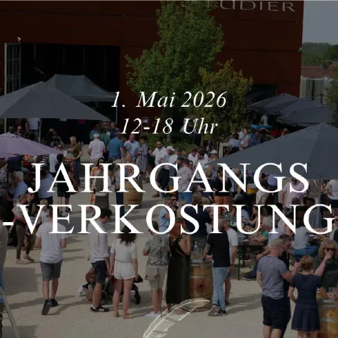 Eine lebendige Veranstaltung im Freien mit vielen Menschen, die sich unter Sonnenschirmen versammeln. Im Hintergrund ist ein Gebäude zu sehen, das zu einer Weinfirma gehört.