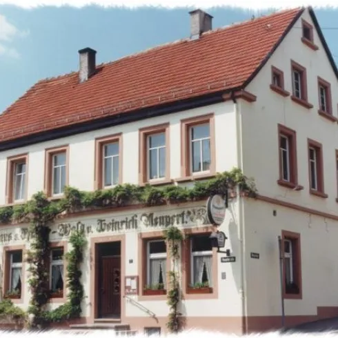 Ein traditionelles Gebäude mit rotem Satteldach und weißen Wänden. Die Fassade ist mit grünen Pflanzen geschmückt, und es gibt ein klassisches Schild an der Wand.