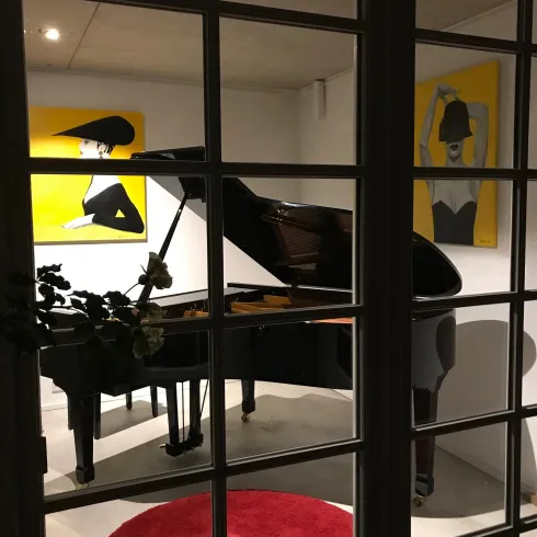 Ein Klavier steht in einem modernen Raum mit gelben Wandbildern. Der Raum ist stilvoll eingerichtet und hat einen runden roten Teppich.