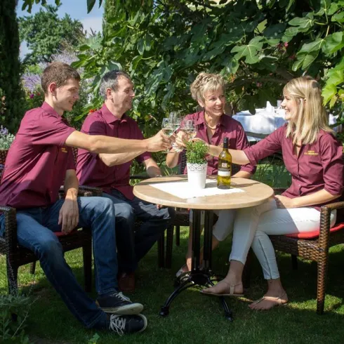 Eine Gruppe von vier Personen stößt in einem Garten mit Glas an. Sie tragen ähnliche rote Hemden und genießen den sonnigen Tag.
