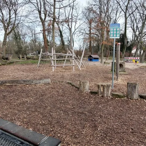 Ein Spielplatz mit einer Rutsche und einer Schaukel. Der Bereich ist umgeben von Bäumen und hat einen Gartenvorplatz aus Holzspänen.