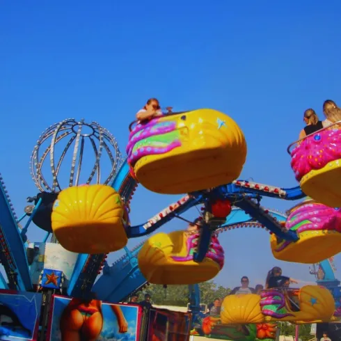 Ein farbenfrohes Karussell mit Kids in den Fahrgeschäften. Der Himmel ist klar und blau, was eine fröhliche Stimmung verbreitet.