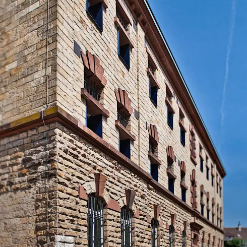 Ein historisches Gebäude mit auffälliger Steinarchitektur und bunten Fenstern. Der klare Himmel ergänzt die attraktive Fassade.