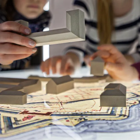 Mehrere Personen arbeiten gemeinsam an einem interaktiven Modell. Holzblöcke werden auf einer Kartenprojektion platziert.