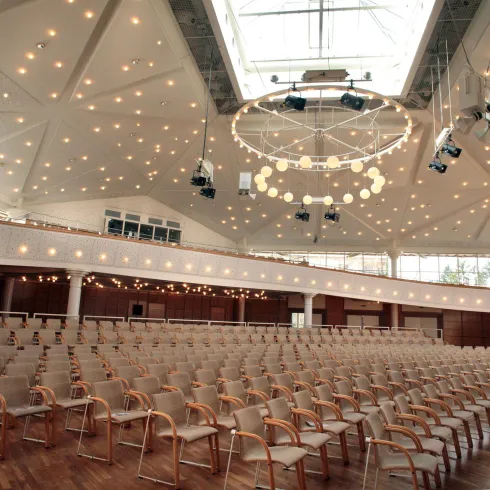 Ein eleganter Veranstaltungsraum mit vielen Stühlen und moderner Beleuchtung. Das große Fenster sorgt für viel Tageslicht.