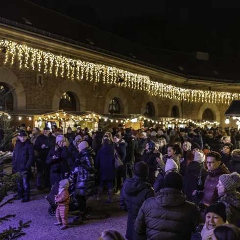 Ein lebhafter Weihnachtsmarkt bei Nacht mit festlicher Beleuchtung. Viele Menschen genießen die stimmungsvolle Atmosphäre um die Stände herum.