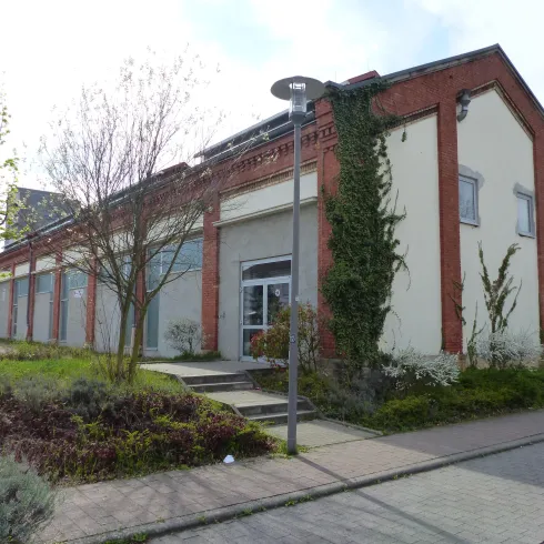 Ein modernes Gebäude mit einem gut gepflegten Außenbereich. Die Fassade ist teilweise mit Pflanzen bewachsen und es gibt Gehwege sowie Straßenbeleuchtung.