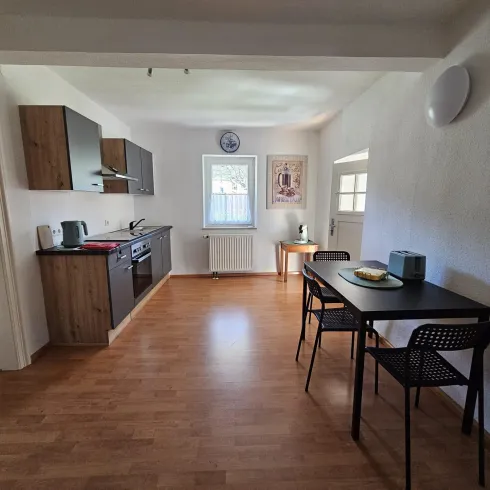 Eine moderne Küche mit Holzschränken und einem kleinen Essbereich. Der Raum ist hell und freundlich, mit viel natürlichem Licht.