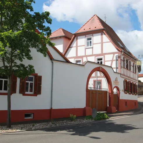 Ein malerisches Dorf mit traditionellen Häusern und einer ruhigen Straße. Der Himmel ist blau mit vereinzelten Wolken.