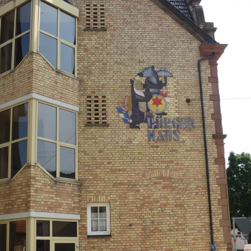 Ein Gebäude mit einer bunten Wandmalerei. Die Fassade besteht aus hellen Ziegelsteinen und hat große Fenster.