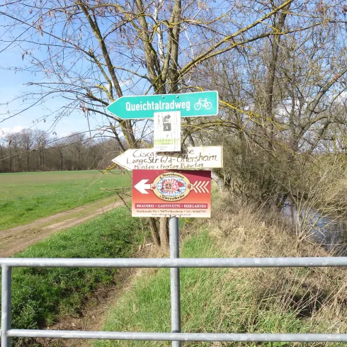 Ein Wegweiser an einem Feldweg mit Fahrradsymbol für den Dunchitalradweg. Im Hintergrund sind Bäume und ein klarer Himmel zu sehen.