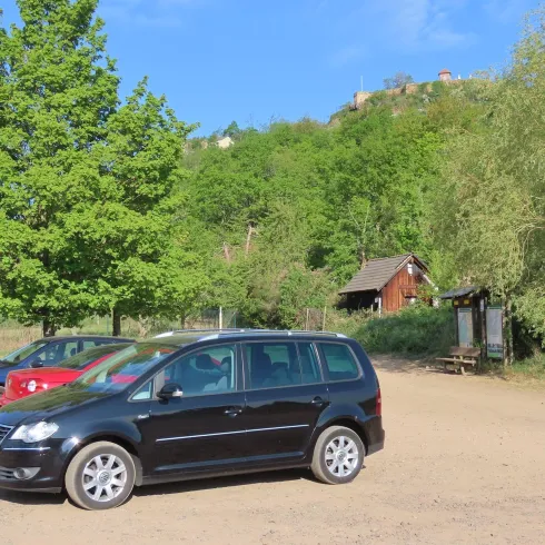 <p>Ein Parkplatz umgeben von Wald und Bäumen. Der Parkplatz ist eine Fläche aus Kies. Auf dem Parkplatz parken bereits drei Auto.</p>