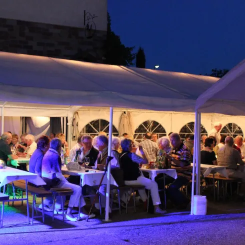 <p>Eine festliche Veranstaltung unter einem Zelt am Abend. Viele Gäste sitzen an Tischen und genießen das Beisammensein.</p>