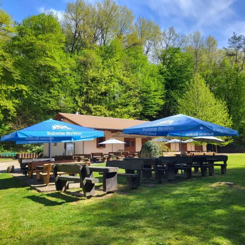 Ein gemütliches Restaurant im Grünen mit großen Sonnenschirmen. Es gibt viele Sitzgelegenheiten auf der Wiese.