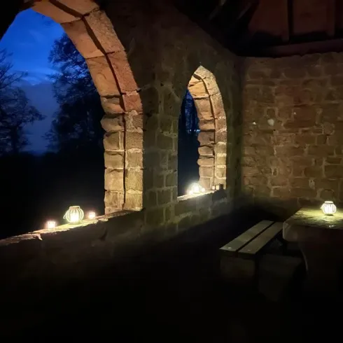 Ein ruhiger Raum mit alten Steinmauern und zwei großen Fenstern. Auf den Fensterbänken stehen Kerzen, die sanftes Licht spenden.